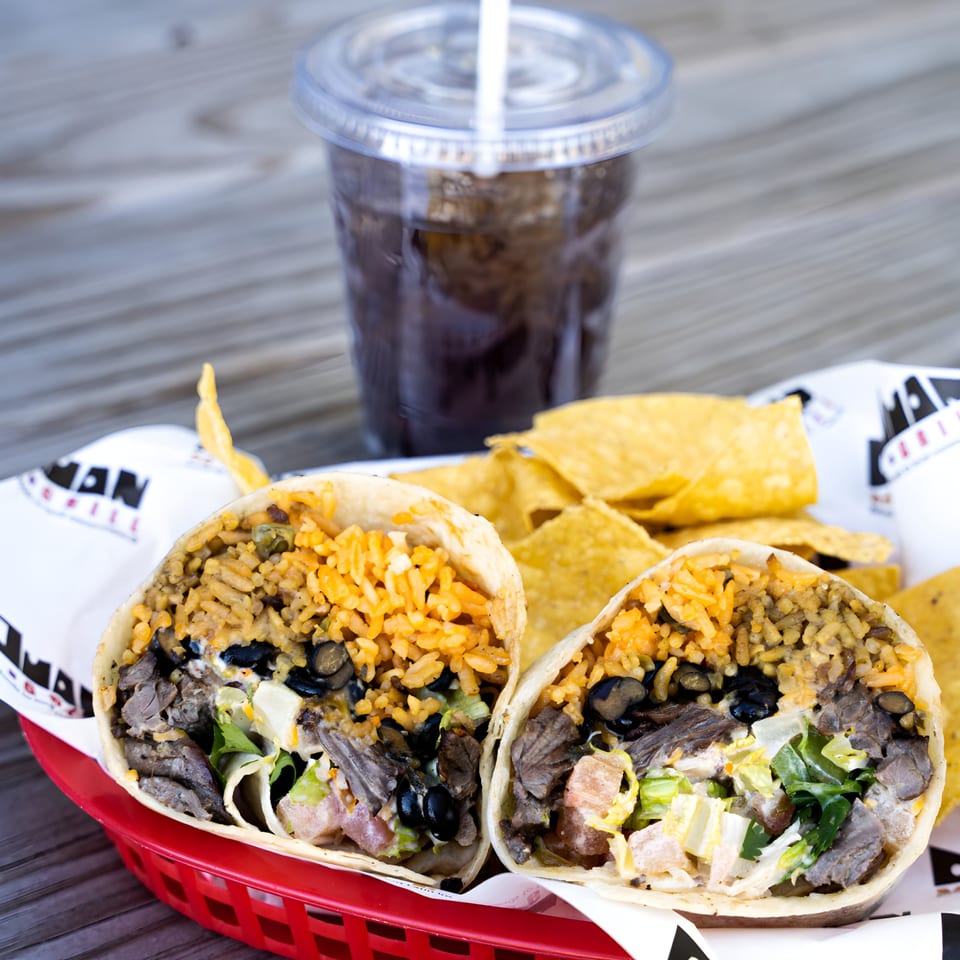 Don Juan Mex Grill burrito cut in half, revealing steak, rice, beans, and lettuce, with chips and a drink.