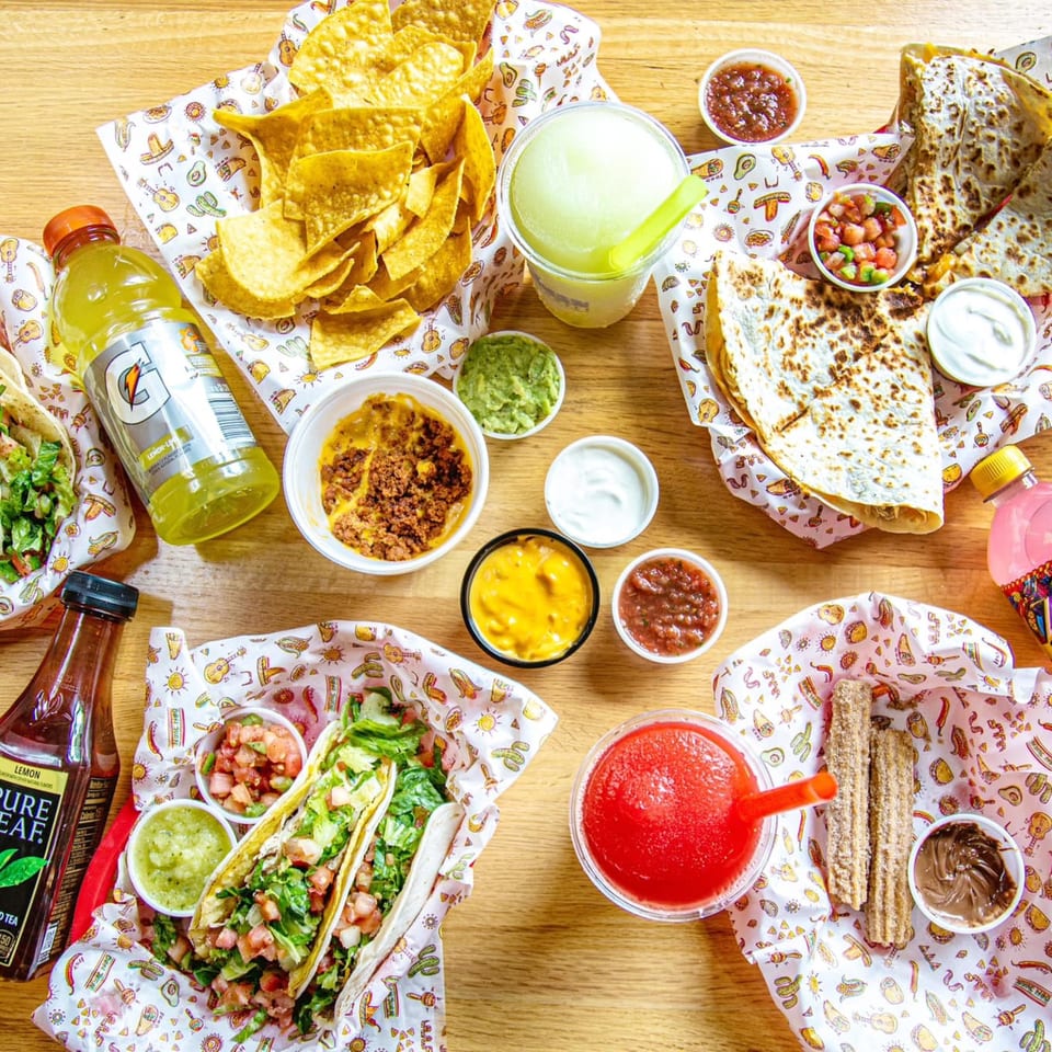 Overhead view of a vibrant Mexican feast with tacos, quesadillas, nachos, churros, and drinks.