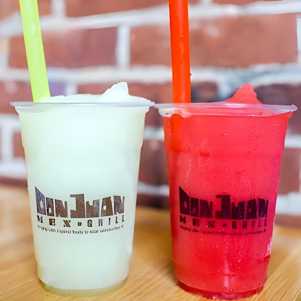 Two Don Juan Mex Grill frozen drinks, one green and one red, with straws against a brick wall.
