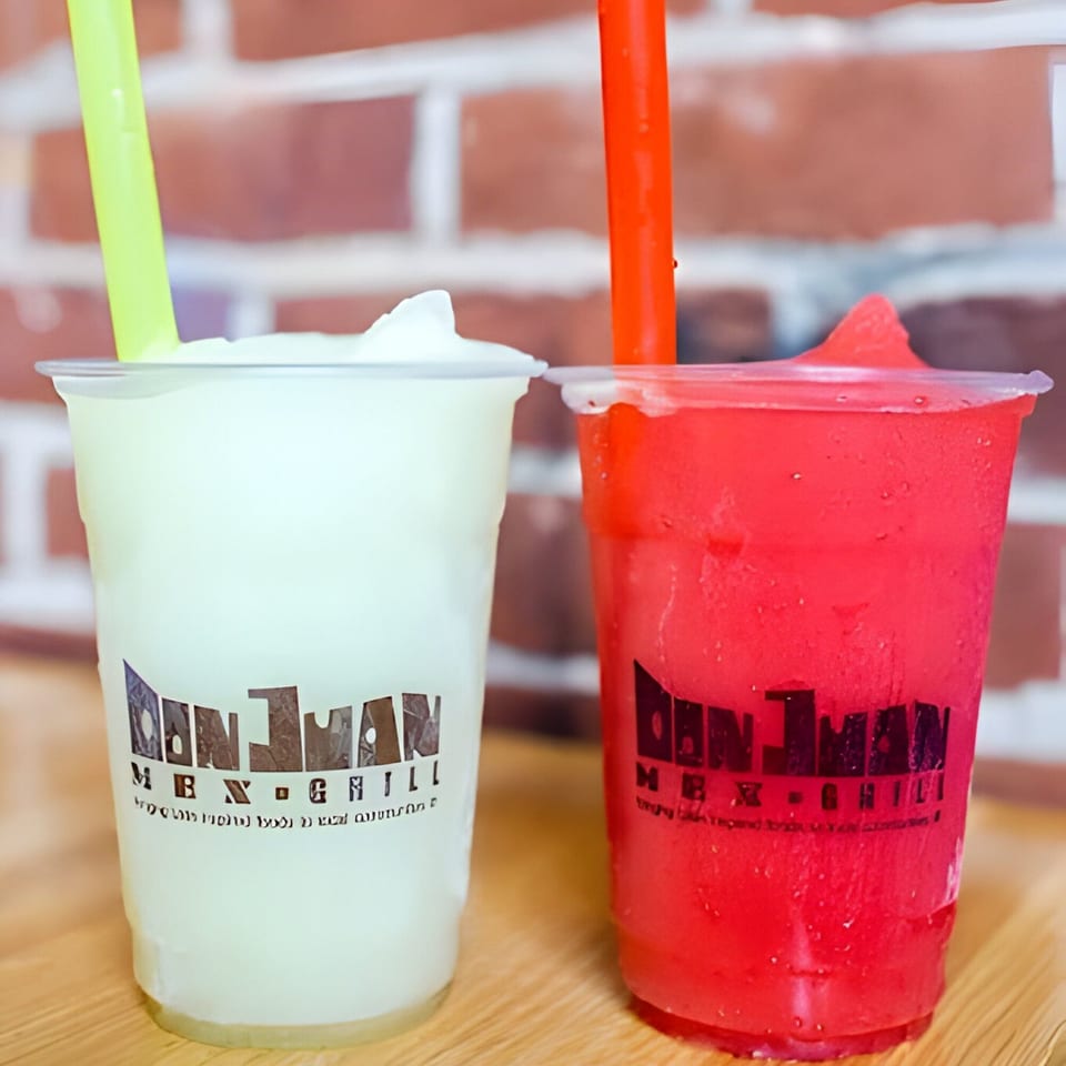 Two Don Juan Mex Grill frozen drinks, one green and one red, with straws against a brick wall.