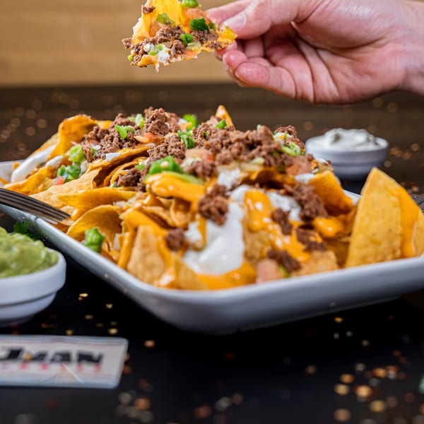 Hand picking up a chip from a large platter of Don Juan Mex Grill nachos with ground beef and cheese.