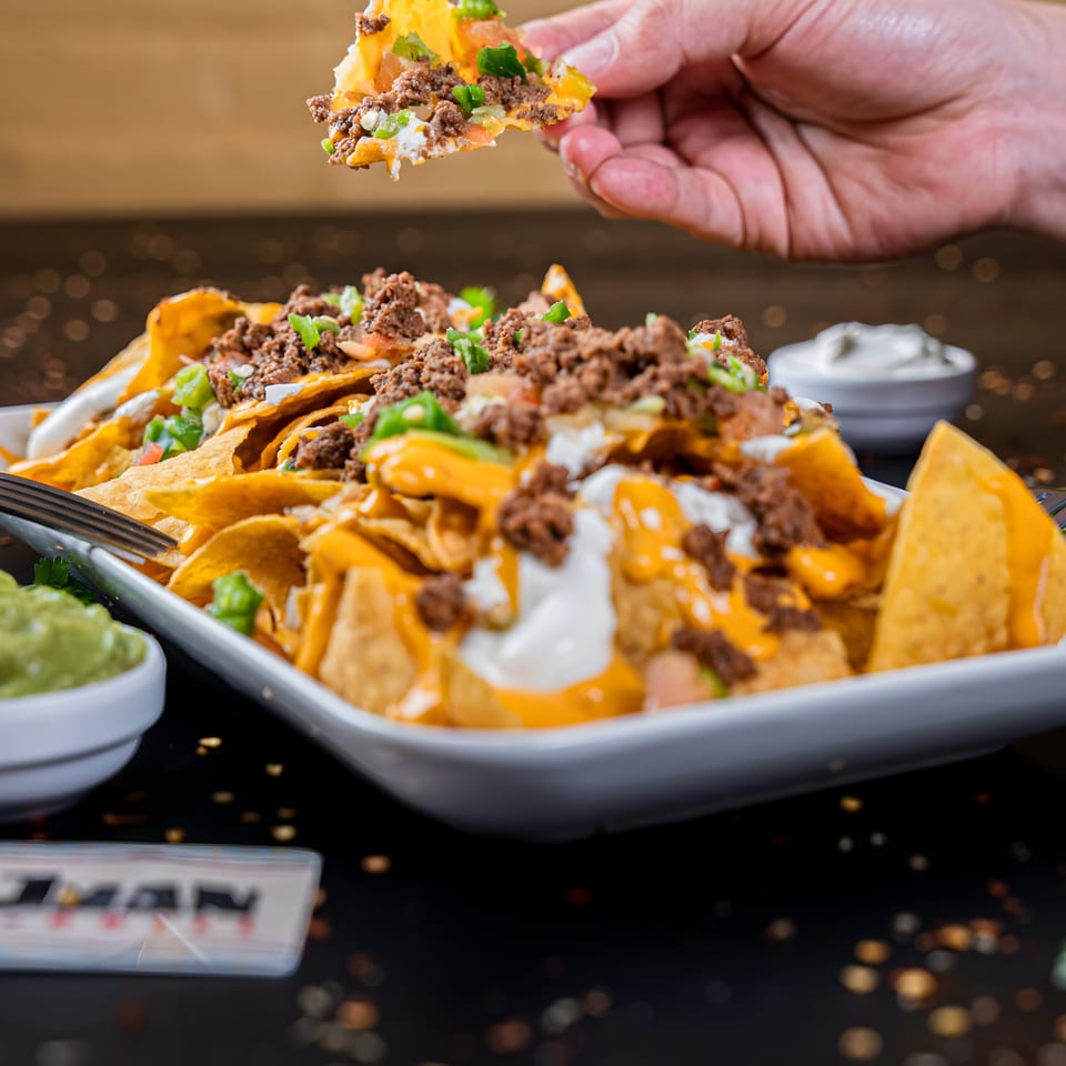 Hand picking up a chip from a large platter of Don Juan Mex Grill nachos with ground beef and cheese.