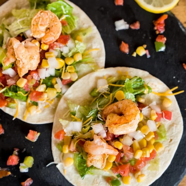 Two Don Juan Mex Grill shrimp tacos with lettuce, corn, tomatoes, onions, and cheese.