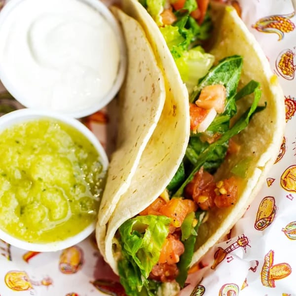 Two Don Juan Mex Grill tacos filled with lettuce and tomatoes, served with guacamole and sour cream.
