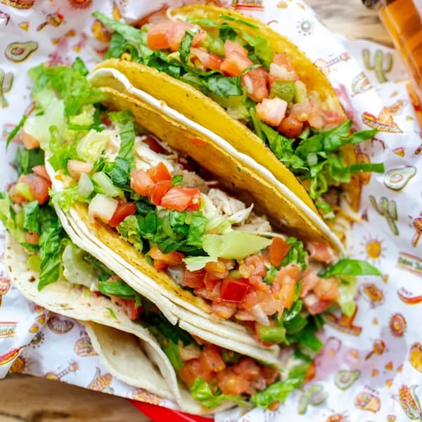 Three Don Juan Mex Grill tacos, one hard shell and two soft, filled with meat, lettuce, and pico de gallo.