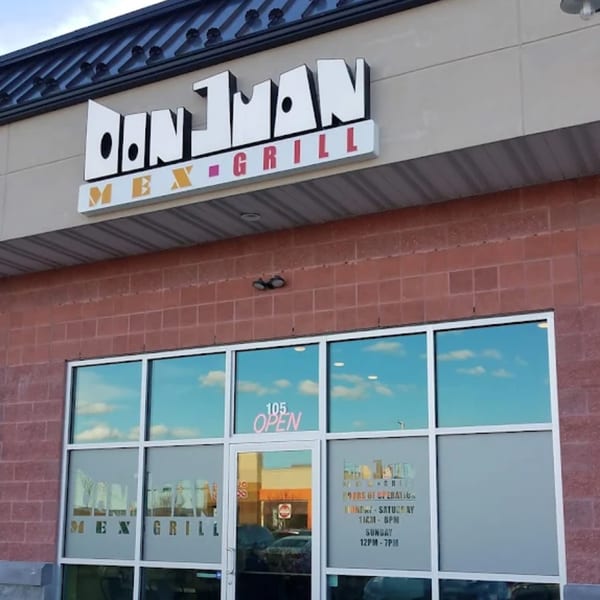 Exterior of Don Juan Mex Grill, featuring its sign, brick facade, and large windows reflecting the sky.