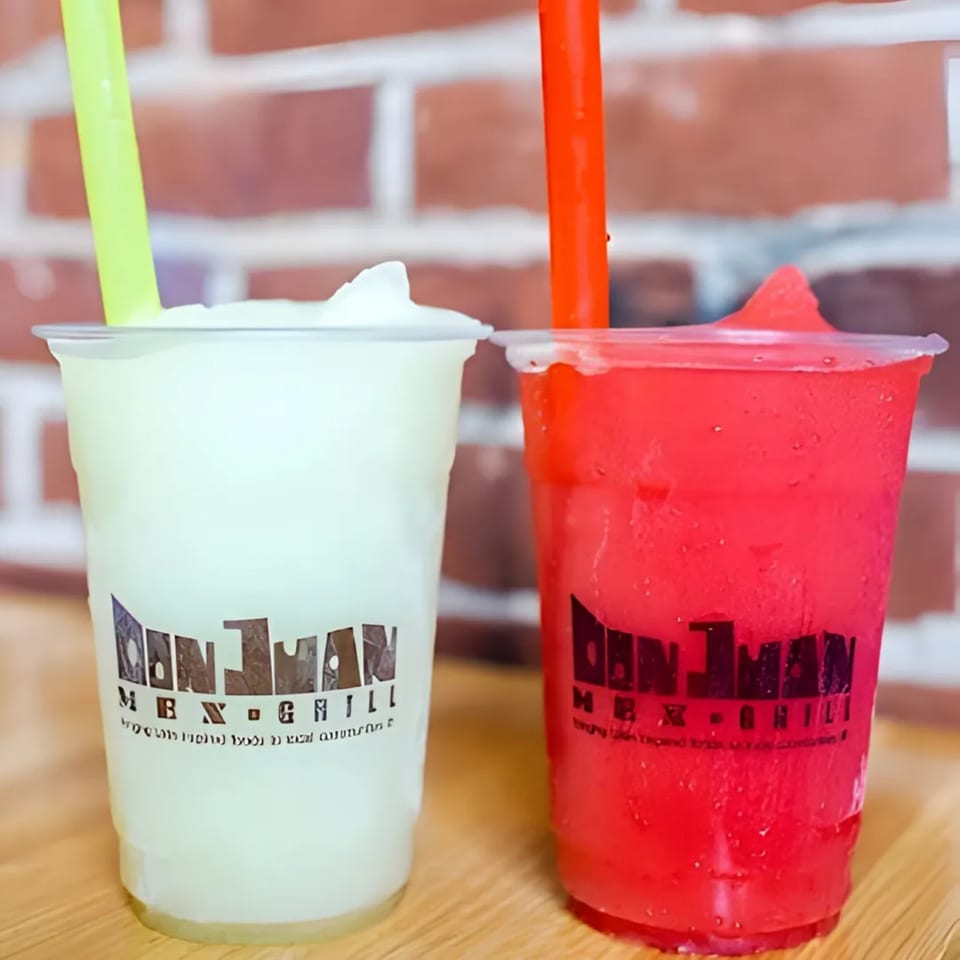 Two Don Juan Mex Grill frozen drinks, one green and one red, with straws against a brick wall.
