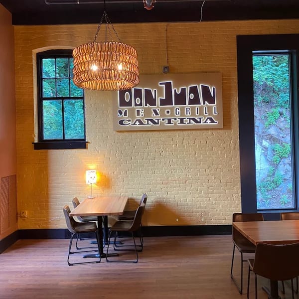 Don Juan Mex Grill Cantina sign on a yellow brick wall, with tables and chairs in the foreground.