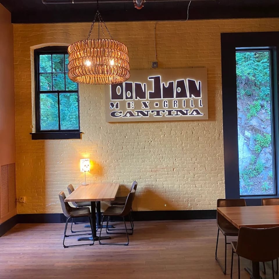 Don Juan Mex Grill Cantina sign on a yellow brick wall, with tables and chairs in the foreground.