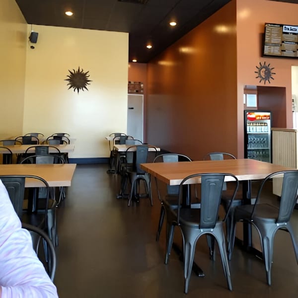 Interior of Don Juan Mex Grill with light wood tables, black chairs, and sun decor on warm-toned walls.