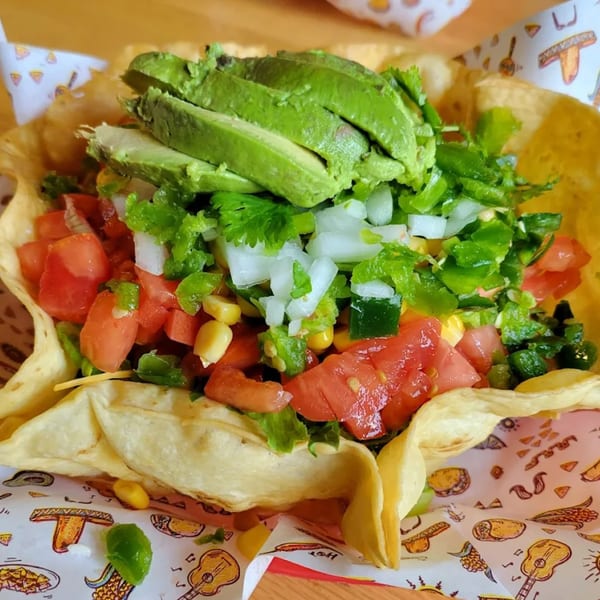 A vibrant Don Juan Mex Grill taco salad with avocado, tomatoes, corn, and onions in a crispy shell.