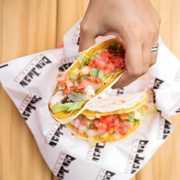 A hand holds a Don Juan Mex Grill taco filled with meat, lettuce, and pico de gallo.