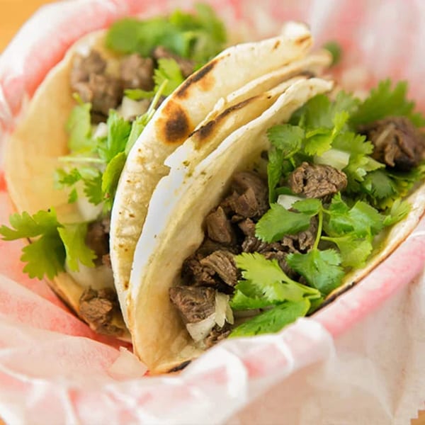 Two Don Juan Mex Grill steak tacos with cilantro and onions in a red and white checkered basket.