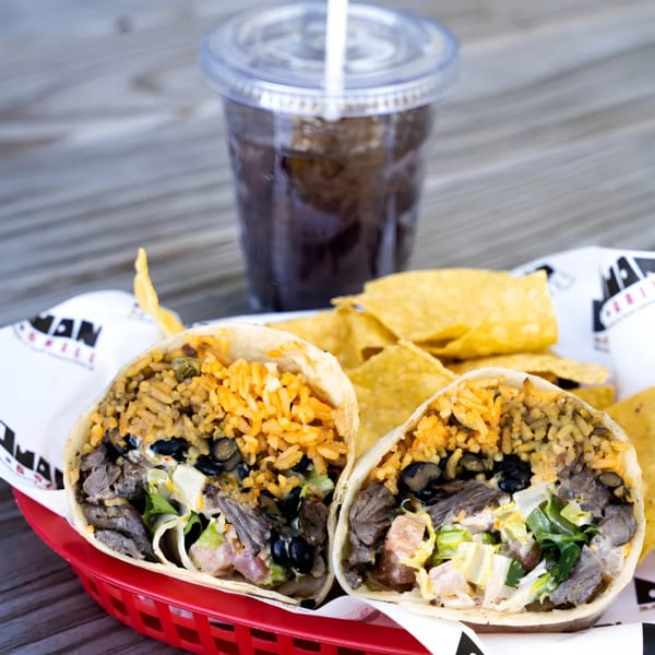 Don Juan Mex Grill burrito, cut in half, revealing rice, beans, meat, and lettuce, with chips and a drink.