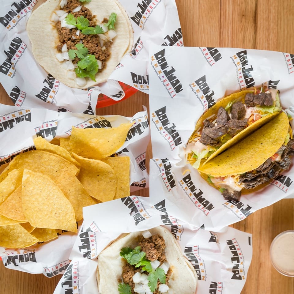Don Juan Mex Grill tacos and tortilla chips on branded paper, with a side of sauce.