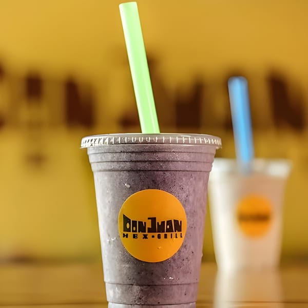 Two Don Juan Mex Grill smoothies with straws, one purple and one white, against a yellow background.