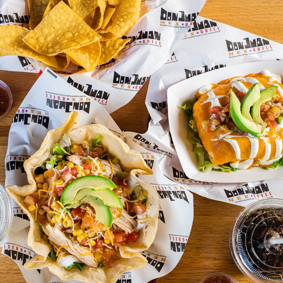 A Don Juan Mex Grill taco salad, burrito, and tortilla chips on branded paper.
